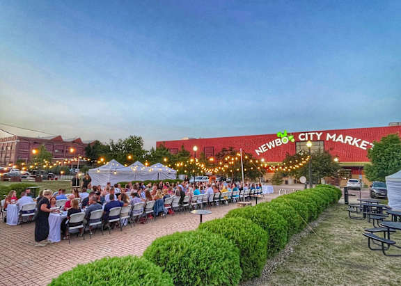 A group of people are sitting at tables outside the Newberry City Market.