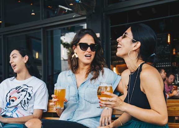 Three women are sitting on a bench, each holding a glass of beer.