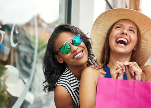 Two women holding shopping bags and smiling.