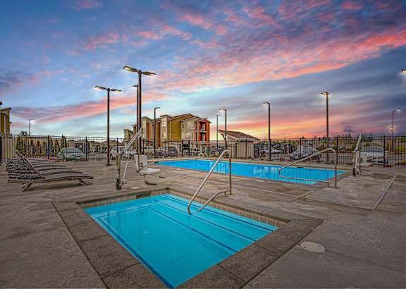 A swimming pool surrounded by a fence and lounge chairs.