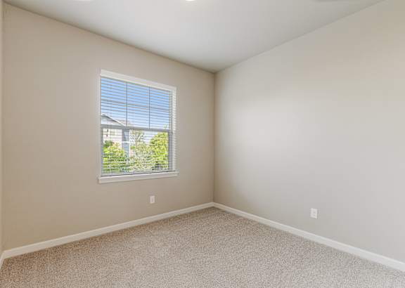 A room with a window showing a view of a house and trees.