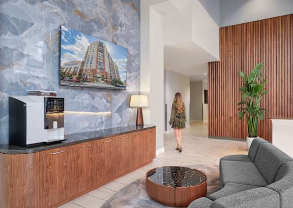 A woman walks through a modern lobby with a coffee machine on the counter.