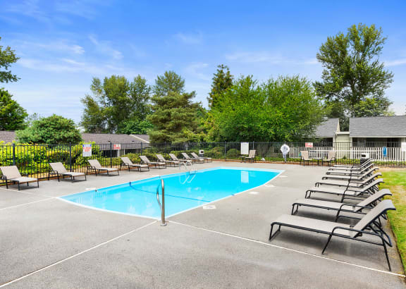 our resort style swimming pool is surrounded by lounge chairs and trees