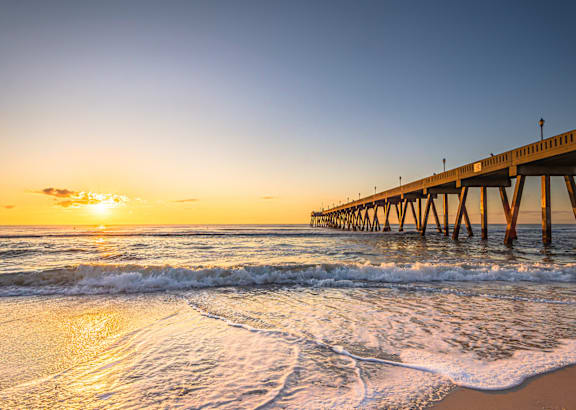 A pier extends into the ocean at sunset.