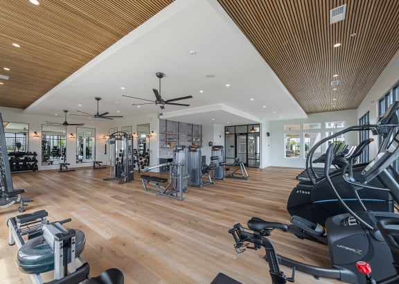 a spacious fitness room with hardwood flooring and ceiling fans