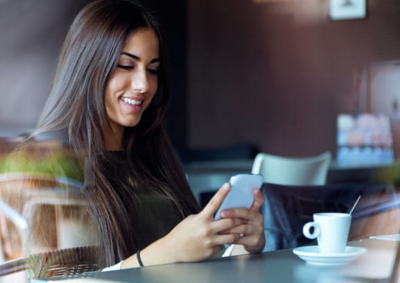 a woman sitting at a table in a coffee shop looking at her cell phone at Tides at Mesa, Mesa, AZ, 85204