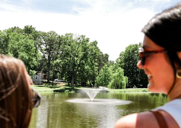 Two women are looking at a pond with a fountain in the middle.