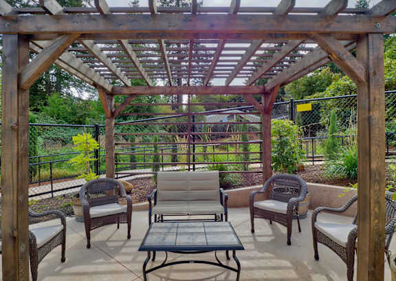 A table and chairs are set up on a patio with a pool and trees in the background.