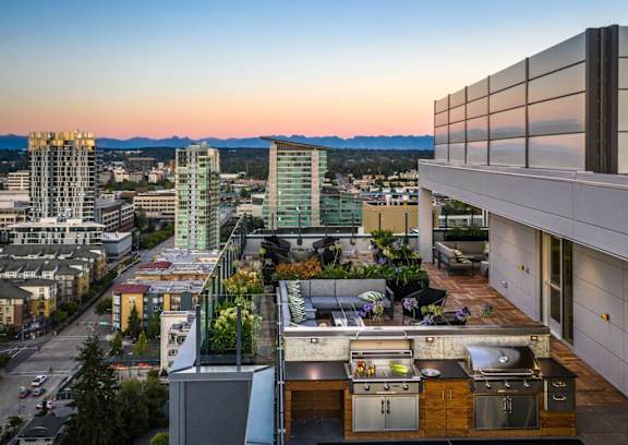 A rooftop patio with a kitchen area overlooks a cityscape.