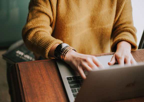 A person in a yellow sweater is typing on a laptop.