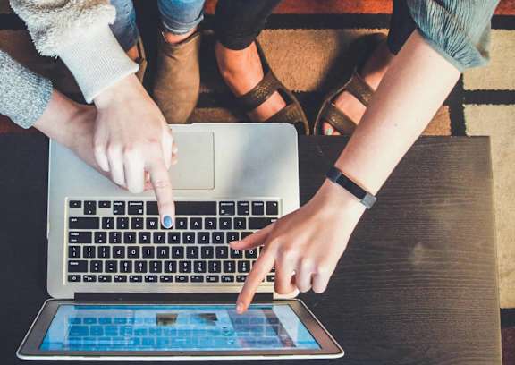 A person in a yellow sweater is typing on a laptop.