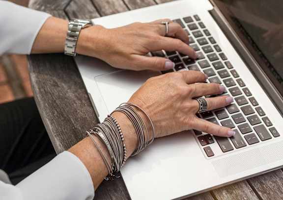 A person in a yellow sweater is typing on a laptop.