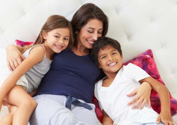 A woman and two children are sitting on a white couch.