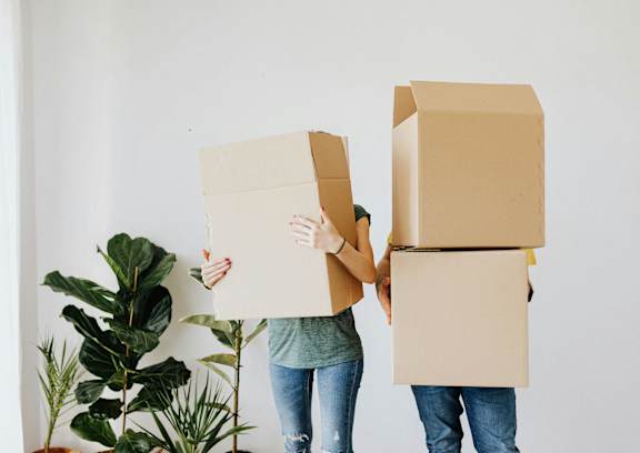 two people holding stacked boxes in a room