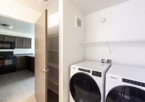 A white wall with a washing machine and dryer in front of it.