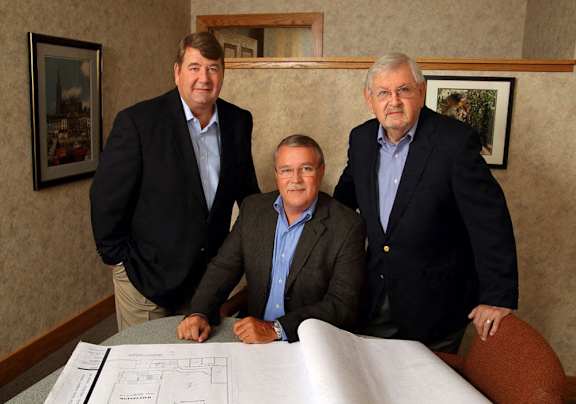 three men standing around a table with a blueprint