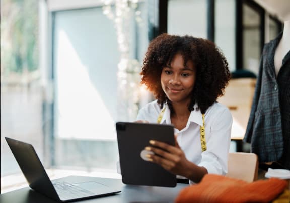 a woman sitting at a table with a laptop and a tablet