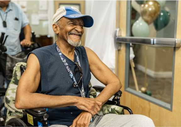 A man in a wheelchair wearing a blue cap and a blue sleeveless shirt with a lanyard around his neck.