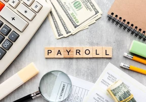 A desk with items related to payroll, including a calculator, money, and a magnifying glass.