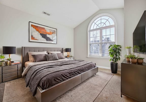 A bedroom with a large bed, a nightstand, and a window.
