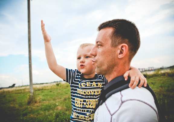 A man and a child are standing in a field with the child pointing upwards.