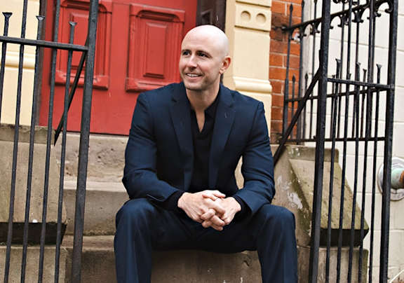 A bald man in a black suit sits on the steps.