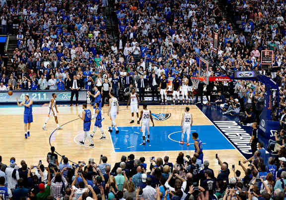 A basketball game is in progress with players in white and blue uniforms on the court.