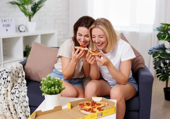 two girls sitting on a couch and eating pizza at Altis Grand Suncoast Apartments in Land o' Lakes, FL 34638