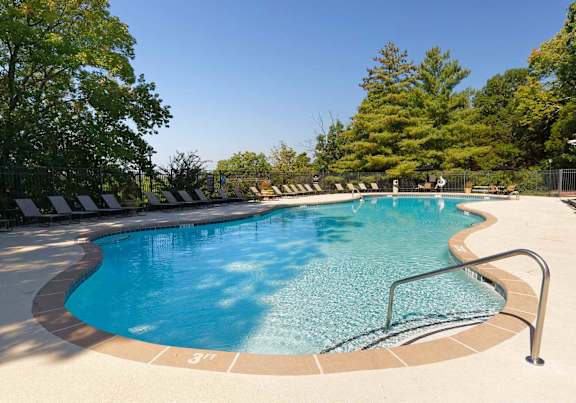 A swimming pool surrounded by trees and lounge chairs.