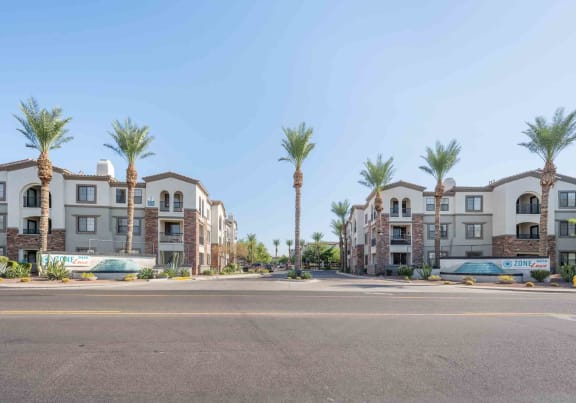 a street view of a row of apartment buildings with palm trees in the background
