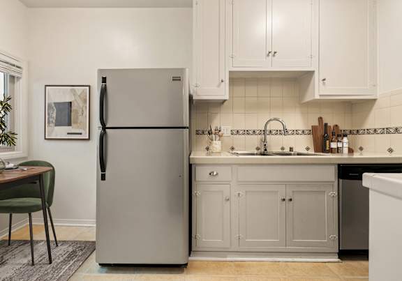 A kitchen with a refrigerator, sink, and cabinets.