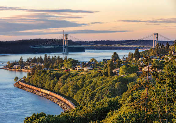 A bridge spans across a body of water with a forested area in the foreground.