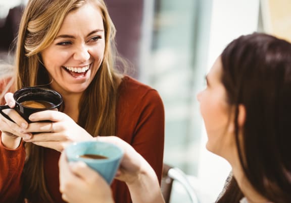 two women sitting at a table laughing and drinking coffee