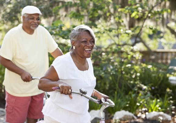an older woman riding a bike with a man walking behind her