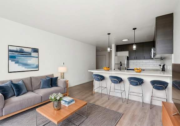 A modern living room with a grey sofa, a wooden coffee table, and a kitchen area in the background.