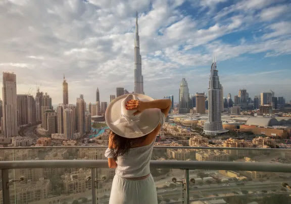A woman in a white dress and hat is looking at the skyline of a city.