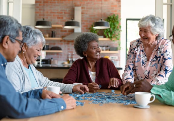 a group of women sit around a table and work on a jigsaw puzzle