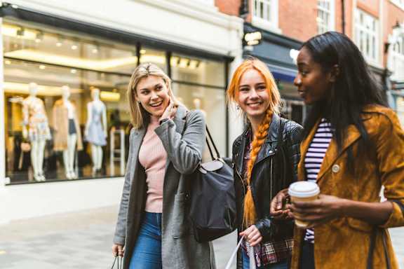 Three women are smiling and holding shopping bags at Compass at City Center, Newport News