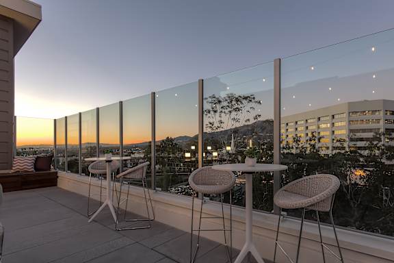 A balcony with a table and chairs overlooking a cityscape at dusk.