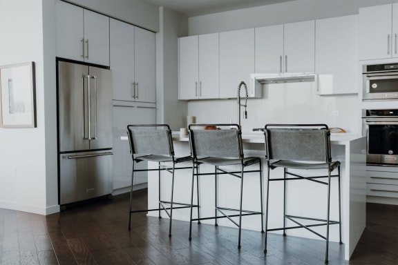 a kitchen with white cabinets and a white island with three stools in front of it