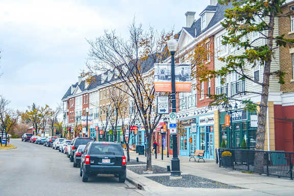 Cars parked on the side of a street with buildings and trees in the background.