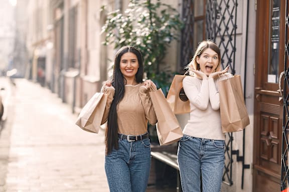 two women walking down a city street holding shopping bags