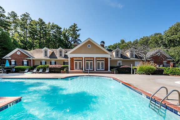 A large outdoor swimming pool surrounded by trees and a building.