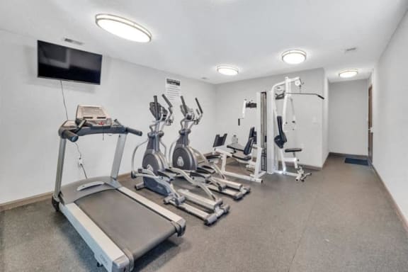 the gym is equipped with cardio machines and a wall mounted tv
