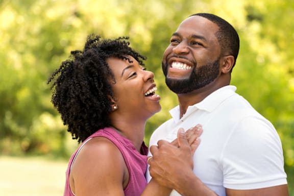 A man and woman are standing close together in a park.