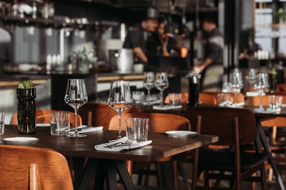 A restaurant with wooden tables and chairs and glasses on the tables.