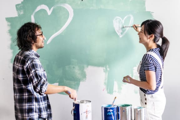a man and woman standing in front of a green wall painting hearts on a wall at The Monroe Apartments, Austin, 78741