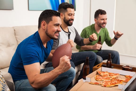 three men sitting on a couch with a football and pizza at The Parker Austin, Pflugerville, 78660