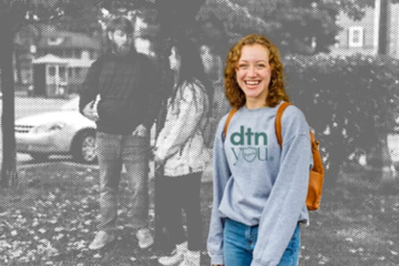 A woman in a grey sweatshirt with the text "dtn you" on it is standing in front of a black and white photo.