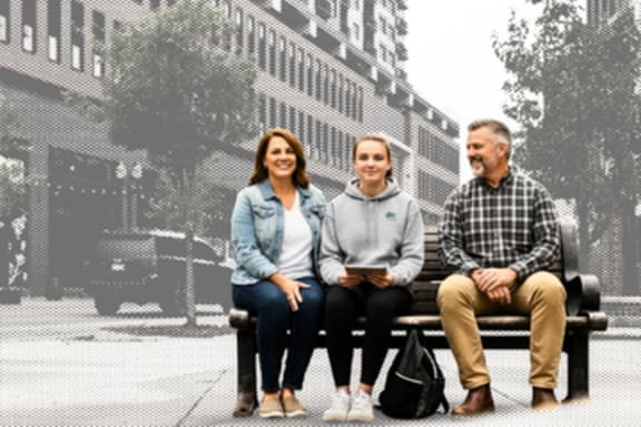 Three people are sitting on a bench in a city setting.